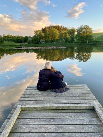 Två kvinnor sitter vid en sjö och stöttar varandra