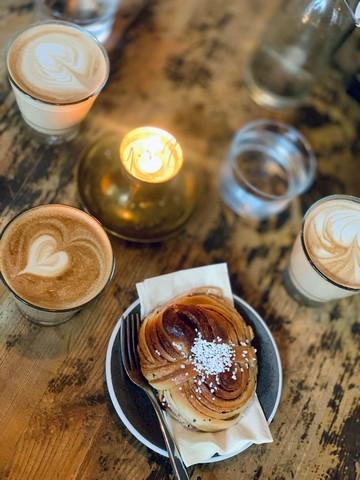  Ett cafébord med en kanelbulle, ett ljus och två koppar kaffe.