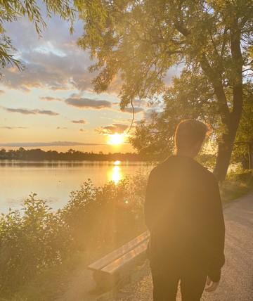 En ung fyr går alene mod solnedgangen langs med en sø 